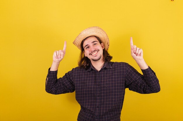 Man wearing typical clothes for party Junina pointing up space for advertising and text