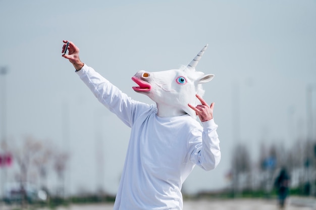 Man wearing unicorn mask taking a photo with smartphone