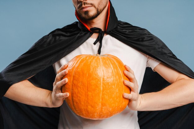 Photo man wearing vampire costume holding a big pumpkin selective focus closeup