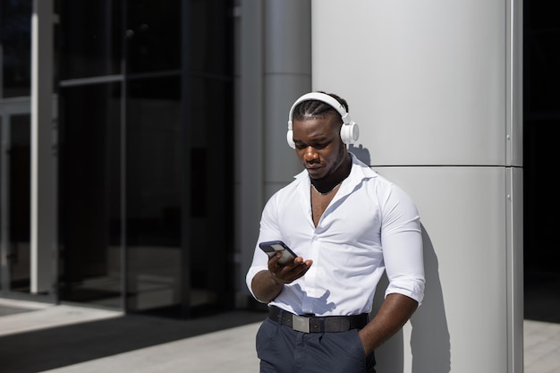 A man wearing a white shirt and black pants is using his phone and looks at his phone.