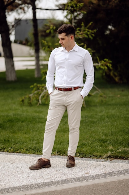 Photo a man wearing a white shirt and brown pants stands on a sidewalk.