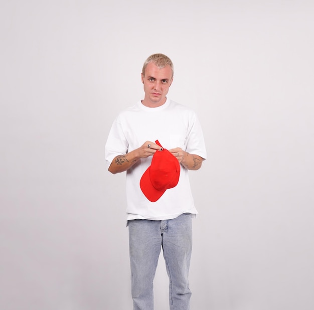 Photo a man wearing a white shirt and jeans holds a red baseball cap.