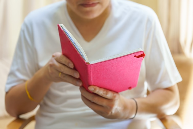 A man wearing white t-shirt sitting and reading a book.