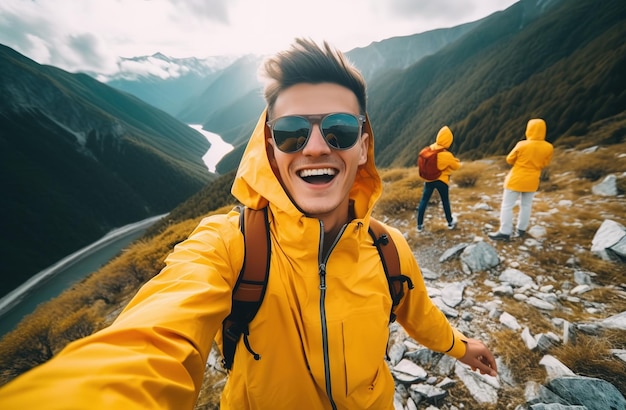 A man wearing a yellow raincoat and sunglasses stands on a mountain top.