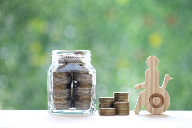 Man on wheelchair and gold coin money in the glass bottle on natural green background