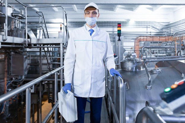 Man in a white robe gloves and mask stands near the production line and holds a white suitcase in his hand at the dairy plant inspector carries out control at the cheese factory