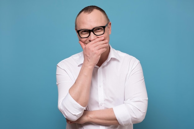 Man in white shirt hiding smile behind palm laughing on funny joke