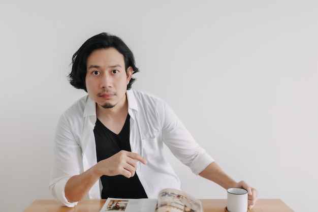 Man in white shirt reading magazine and drink coffee on wooden table