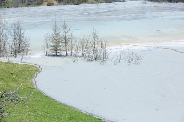 A man in a white shirt stands in front of a frozen lake with a sign that says'lake of water '