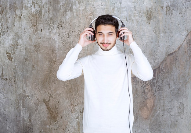 Photo man in white sweater wearing headphones and listening the music.