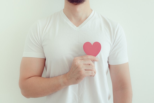 Man in white t-shirt shows pink heart shape in concept of love and Valentine.