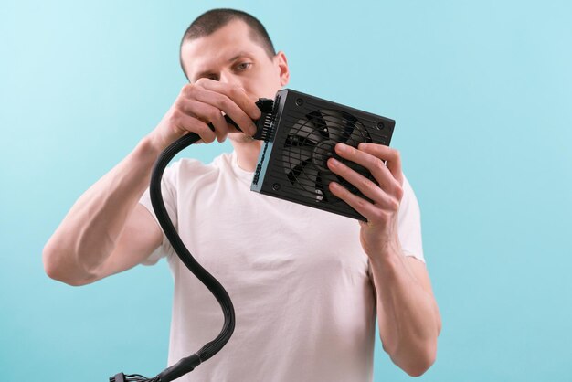 A man in a white tshirt connecting a pin cable to a computer power supply on a blue background Hand Electricity Electronic Supply Component Connection Fixing Repair Unit Electric