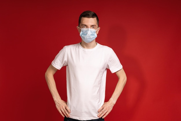 A man in a white Tshirt and protective mask stands against a red background