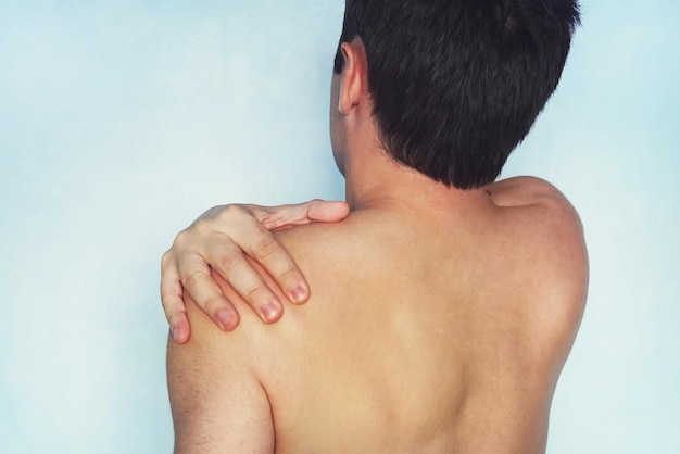 A man who has a shoulder pain low back pain A young guy with a naked body holds his arm a sore shoulder on a blue background athlete with a fracture or dislocation of the shoulder