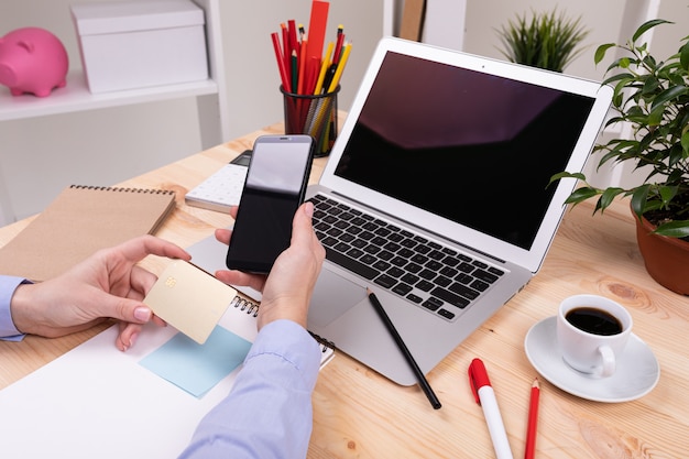 A man who works with laptop, calculator, pens, pencils, card, phone and a plant on his desktop in his office