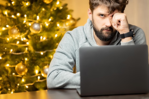 A man whose tired shaggy sits at a laptop on Christmas night