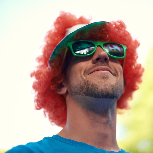 Man wig and sunglasses with nature sky and festival for fun joy and celebration Person summer and concert with low angle smile and happy for event party or sunshine for celebration and closeup