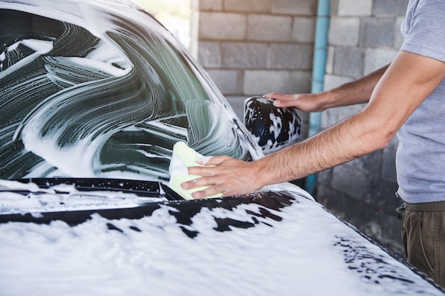 A man wipes the foam on the car with a rag. car wash