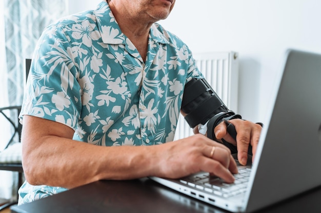 Man with adjustable articulated elbow orthosis typing on laptop keyboard