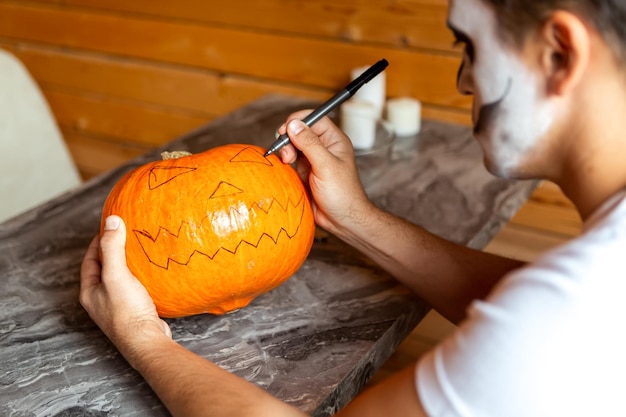 Man with artistic spooky makeup standing prepare for Halloween by carving pumpkins