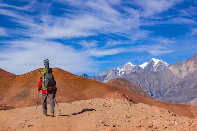 A man with a backpack and a guitar goes on the road to the mountains of Nepal. Rear view.