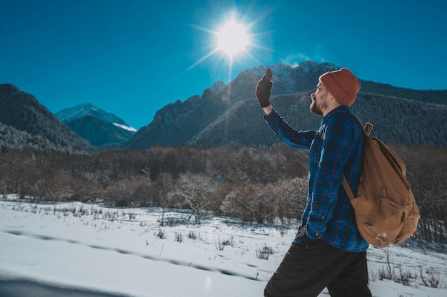 Man with backpack trekking in mountains. Cold weather, snow on hills. Winter hiking. Sun and snow