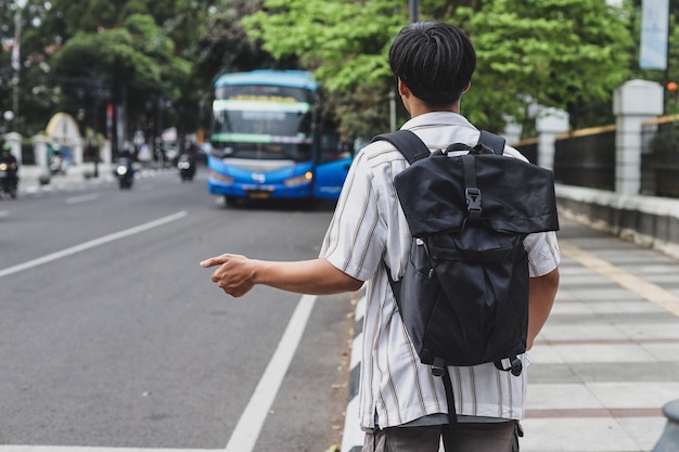 man with backpack waiting for tourist bus for strolling around the city at the road side