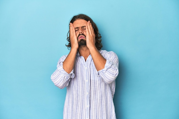 Man with beard in blue striped shirt crying unhappy with something agony and confusion concept