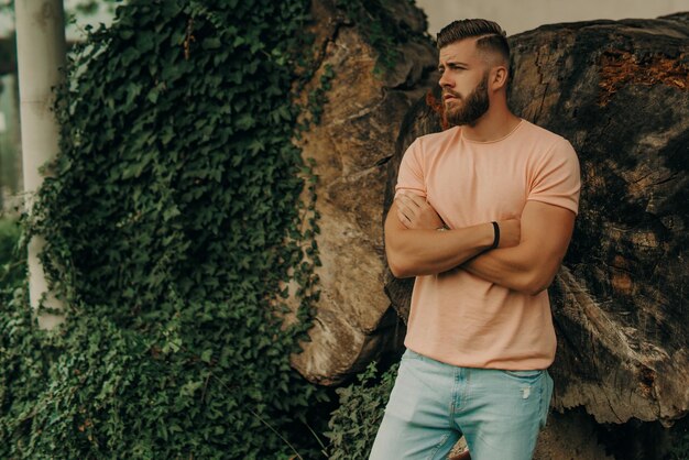 Man with beard and pink shirt posing in green park.