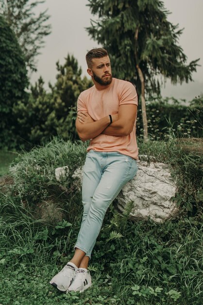 Man with beard and pink shirt posing in green park.