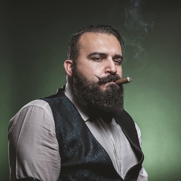 Man with a beard smoking a cigar, looking at the camera.