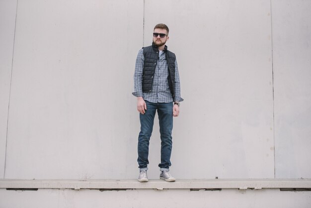 A man with a beard and sunglasses in a plaid shirt and waistcoat posing on the street