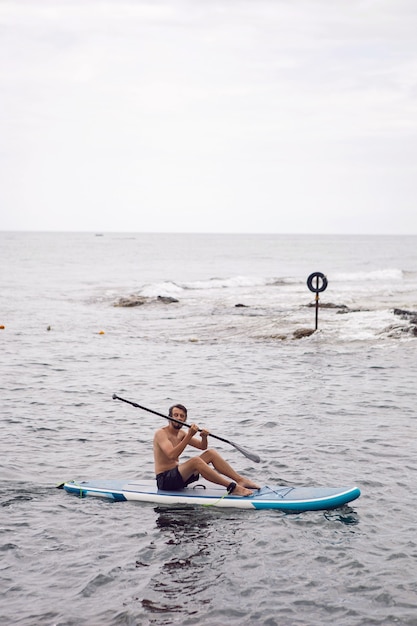 Man with a beard swims on stand up paddle board on a quiet blue ocean. Sup surfing in water