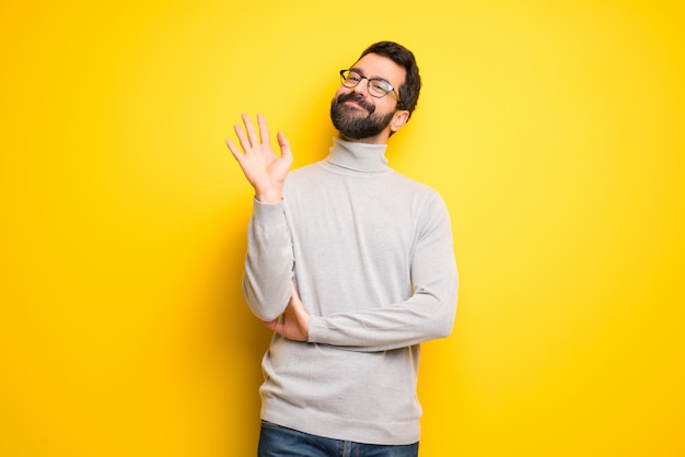 Photo man with beard and turtleneck saluting with hand with happy expression