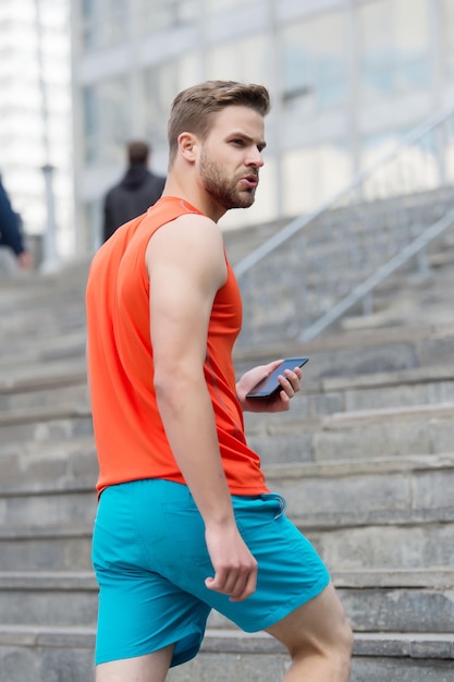 Man with beard walks with smartphone, urban background with stairs. Man using gps navigation on smartphone. gps navigation concept. Sportsman use navigation during orienteering competition.