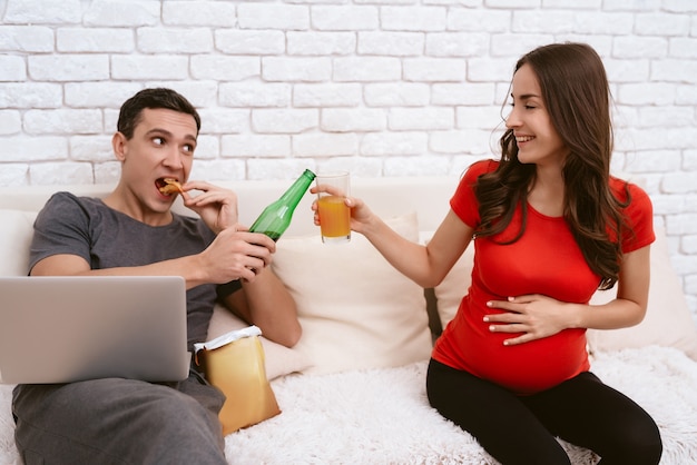 A man with beer while a girl with juice clink glasses.