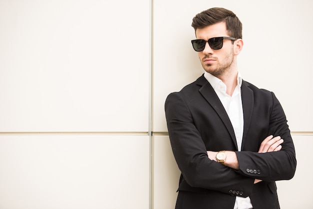 Man with black glasses is posing in front of a wall.