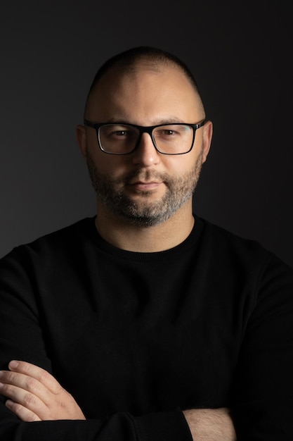 A man with black-rimmed glasses poses with his arms crossed on his chest