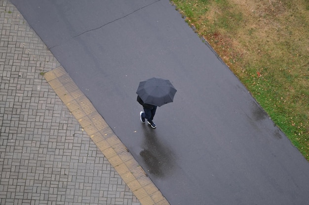 Man with a black umbrella walks along the road top view