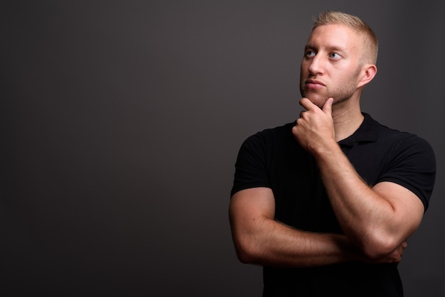 Man with blond hair wearing black polo shirt on gray wall