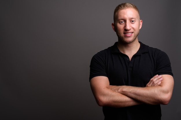 Man with blond hair wearing black polo shirt on gray wall