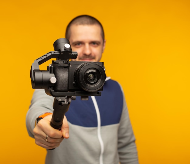 Man with camera on gimbal recording something at orange background and looking in camera