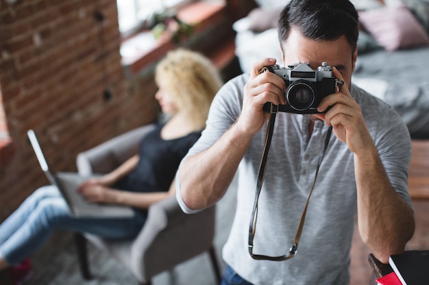 Man with a camera taking a picture with a woman sitting with a laptop