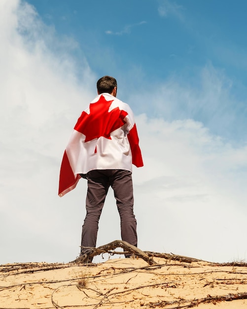 A man with a Canadian flag stands on the sand skies on the background