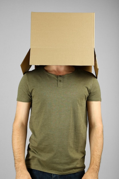 Man with cardboard box on his head on grey background