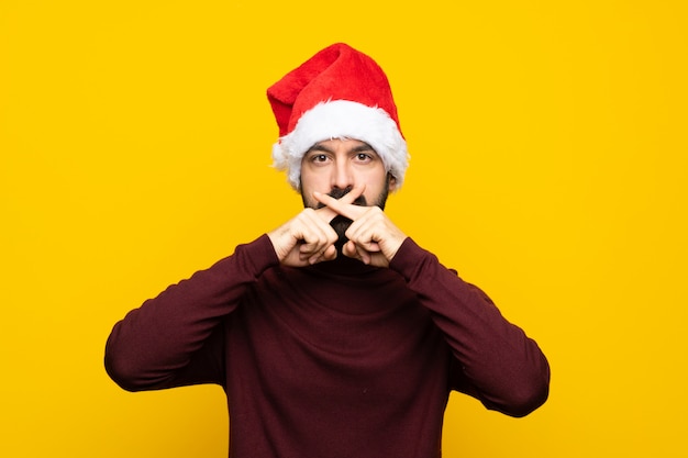 Man with christmas hat over isolated yellow wall showing a sign of silence gesture