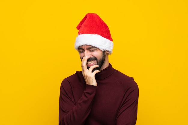 Man with christmas hat over isolated yellow wall smiling a lot