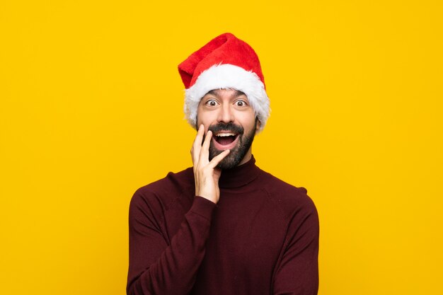 Man with christmas hat over isolated yellow wall with surprise and shocked facial expression