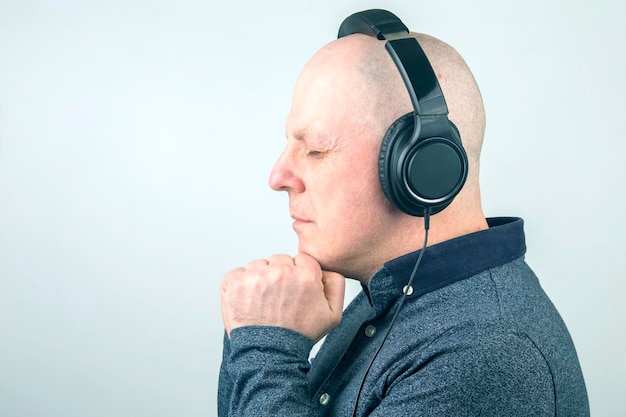 Man with closed eyes listens to music with headphones on a light background