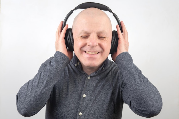 Man with closed eyes listens to music with headphones on a light background